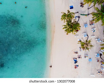 Beautiful beach with white sand palm trees and clear blue sea. People sunbathe and swim, top view