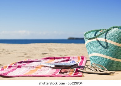 Beautiful beach, white sand, sunny day with magazines towel and beach accessories. - Powered by Shutterstock