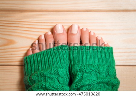 Beautiful beige pedicure. Legs in green knitted socks on a wooden floor