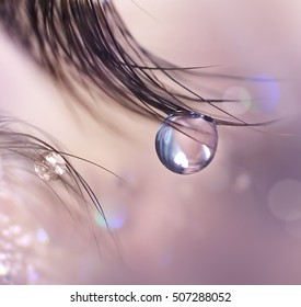 Beautiful big tear or a drop of dew on the eyelashes close up. Soft focus, soft blurred background in pastel colors, circular bokeh. Eye macro eyelashes. Romantic artistic image.