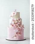 Beautiful big three-tier cake with velvet chocolate coating decorated with pink sugar orchid flowers. Wedding cake on the white background