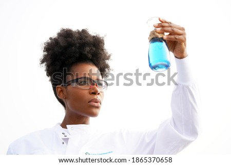 Beautiful black actual scientist with hair up performs laboratory experiments with chemicals and beakers while wearing protective glasses and clothing