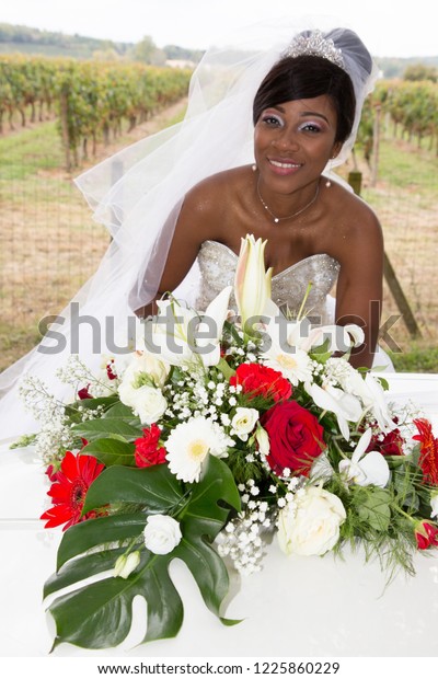 Beautiful black african bride with dark\
skin in wedding car with large bouquet\
flowers