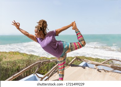 Beautiful Black, African, Or Carribean Woman Practicing Wellness And Yoga Poses At Resort Or Hotel Outdoors Overlooking Gorgeous Beach And Ocean.