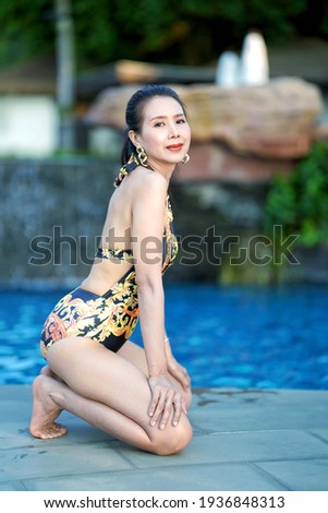 Beautiful woman​ in​ black bikini sitting by swimming​ pool, summer​ vacation, leisure activities.                      