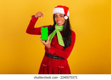 Beautiful black Brazilian woman, dressed in christmas clothes, santa claus, smartphone and showing green chroma screen. - Powered by Shutterstock