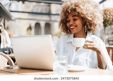 Beautiful black businesswoman sitting in restaurant or cafe bar and using her laptop computer for online communication or corporate video chat. Bright sunny day. - Powered by Shutterstock