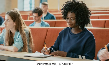 Beautiful Black Female Student Sitting Among Her Fellow Students in the Classroom, She's Writing in the Notebook and Listens to a Lecture.