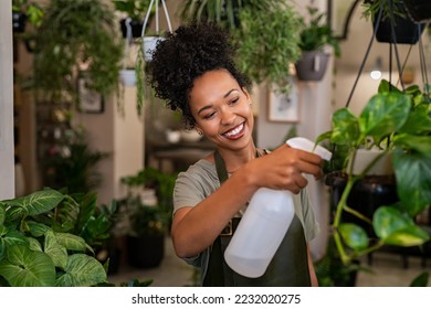 Beautiful black florist taking care of plants while spraying it with water. African american owner working and spraying water plants in store. Happy and smiling florist watering plants in shop. - Powered by Shutterstock