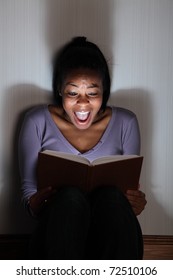 Beautiful Black Girl Sitting On The Floor Screaming While Reading A Horror, Or Scary Thriller Book.