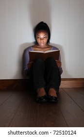 Beautiful Black Girl Sitting On The Floor Reading A Horror, Or Scary Thriller Book.