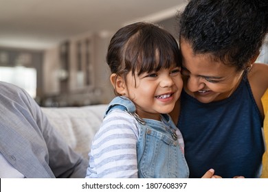 Beautiful black mother embracing little girl sitting on couch with copy space. Cute daughter hugging african mother and smiling together. Happy mom jokes with her kid at home and playing together. - Powered by Shutterstock