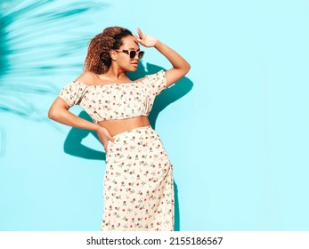 Beautiful Black Woman With Afro Curls Hairstyle. Smiling Model Dressed In Summer Hipster Clothes. Sexy Carefree Female Posing Near Blue Wall In Studio. Tanned And Cheerful. In Sunglasses