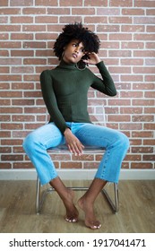 Beautiful black woman with afro hair sitting on the chair against the brick wall background