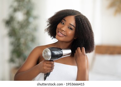 Beautiful black woman in bath towel using hairdryer after shower at home. Pretty African American lady drying her hair, making hairdo, taking care of herself. Everyday hygiene concept - Powered by Shutterstock