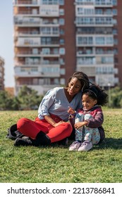 Beautiful Black Woman With Braids Sitting In The Grass With Her Young Daughter And Enjoying Sunny Day.