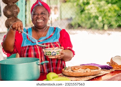Beautiful black woman of the Garífuna ethnic group smiles at the camera as she puts the hot soup on the plate. - Shutterstock ID 2321557563