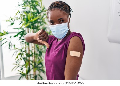 Beautiful Black Woman Getting Vaccine Showing Arm With Band Aid With Angry Face, Negative Sign Showing Dislike With Thumbs Down, Rejection Concept 