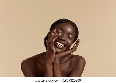 Beautiful Black Woman. Happy young girl touch her clean face and looking at camera. Concept of face skin care. Isolated on beige background. Studio shoot