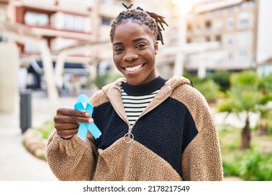 Beautiful Black Woman Holding Blue Ribbon Looking Positive And Happy Standing And Smiling With A Confident Smile Showing Teeth 