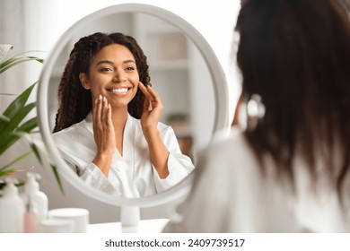 Beautiful black woman at home admiring her reflection in the mirror, african american lady smiling and gently touching her face, capturing a serene moment of self-acceptance and happiness - Powered by Shutterstock