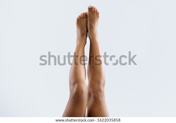 Beautiful black woman lifting her legs up in air,\
grey background,\
cropped