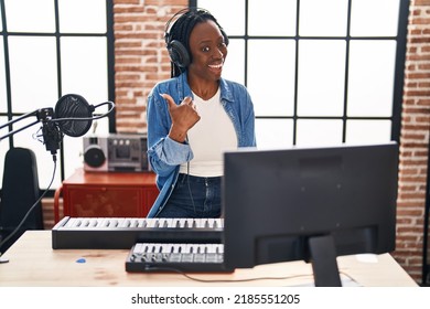 Beautiful Black Woman Playing Piano At Music Studio Pointing Thumb Up To The Side Smiling Happy With Open Mouth 