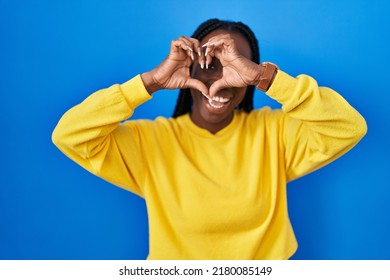 Beautiful Black Woman Standing Over Blue Background Doing Heart Shape With Hand And Fingers Smiling Looking Through Sign 