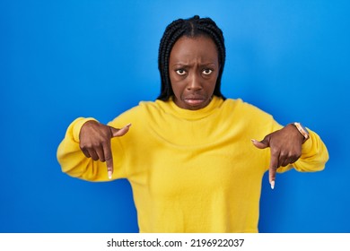 Beautiful Black Woman Standing Over Blue Background Pointing Down Looking Sad And Upset, Indicating Direction With Fingers, Unhappy And Depressed. 