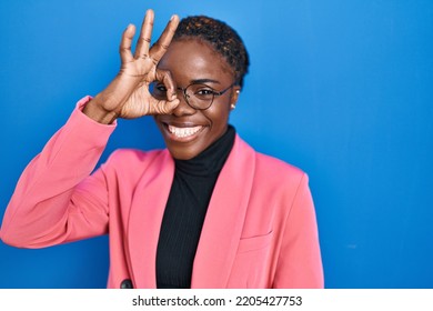 Beautiful Black Woman Standing Over Blue Background Doing Ok Gesture With Hand Smiling, Eye Looking Through Fingers With Happy Face. 