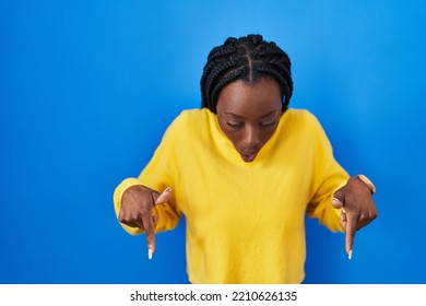 Beautiful Black Woman Standing Over Blue Background Pointing Down With Fingers Showing Advertisement, Surprised Face And Open Mouth 