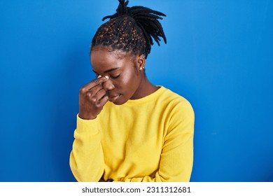 Beautiful black woman standing over blue background tired rubbing nose and eyes feeling fatigue and headache. stress and frustration concept.  - Shutterstock ID 2311312681