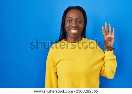 Beautiful black woman standing over blue background showing and pointing up with fingers number four while smiling confident and happy. 