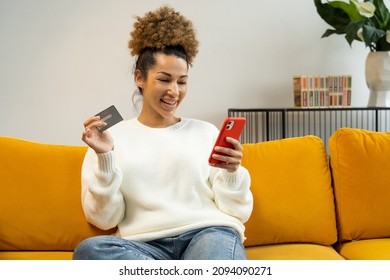 Beautiful Black Woman Using A Credit Card For Shopping And Banking Online With A Mobile Phone While Sitting At Home On The Couch
