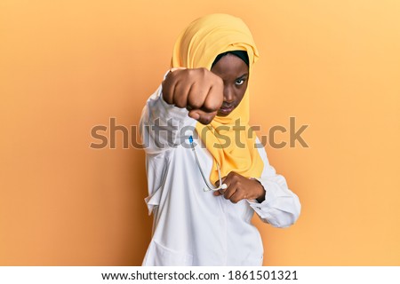 Beautiful black woman wearing doctor uniform and hijab showing and pointing up with fingers number four while smiling confident and happy. 