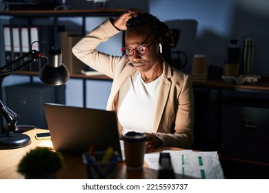 Beautiful black woman working at the office at night confuse and wonder about question. uncertain with doubt, thinking with hand on head. pensive concept.  - Shutterstock ID 2215593737