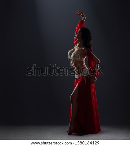 beautiful black-haired girl in a red ethnic dress dancing oriental dances on stage in the dark