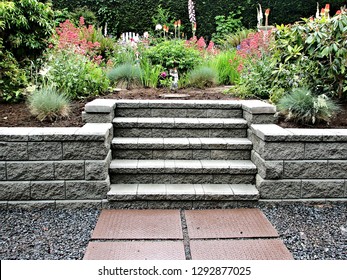 A beautiful block retaining wall in gray color with integrated staircase into existing garden landscaped with perennial flowers and shrubs  - Shutterstock ID 1292877025