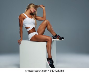 Beautiful blond female posing on white box in studio over grey background.