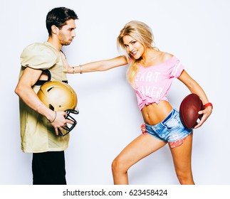 Beautiful Blond Girl Cheerleader With A Ball Is Attacking A Quarterback. A Player In A Football Uniform With A Helmet Stands In Defense. Super Bowl. Sport. Footy.