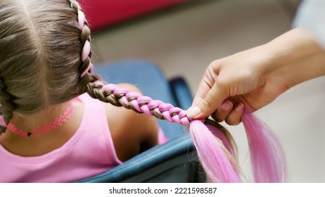 Beautiful blond girl, of seven years old, braided two pigtails, do a hairstyle with pink locks of hair in a beauty salon, a hairdresser's salon, in front of a large mirror. a little princess. High