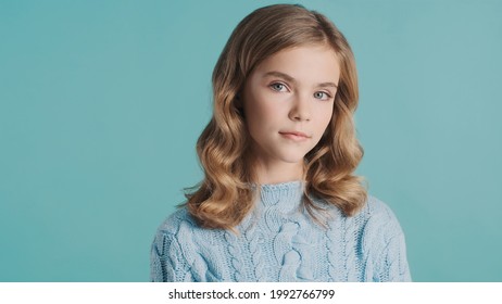Beautiful blond haired teenager girl intently looking in camera posing over colorful background. Studio shot
