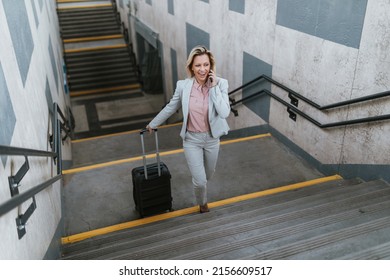 A Beautiful Blond Middle-aged Businesswoman Talking On Mobile Phone While Walking Up Subway Exit Stairs.