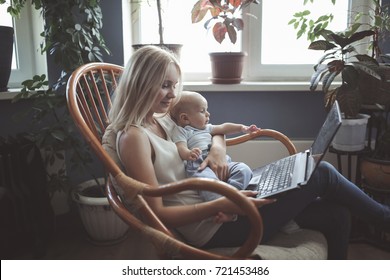 beautiful blond mom with baby son on hands working on a laptop in a chair made of rattan home. concept a working mom, emotional lifestyle, selective  focus and toning