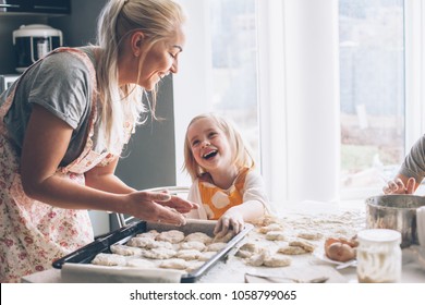 Beautiful blond mom teaching her daughter cooking on the kitchen. Parent making everyday breakfast together with child. Family at home lifestyle photo. - Shutterstock ID 1058799065
