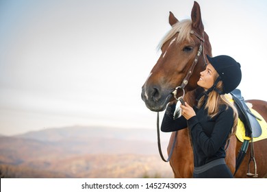 beautiful blond professional female jockey standing near horse. woman horse rider is preparing to equitation. girl and horse. equestrian sport concept. riding vacation.friendship with horse.copy space