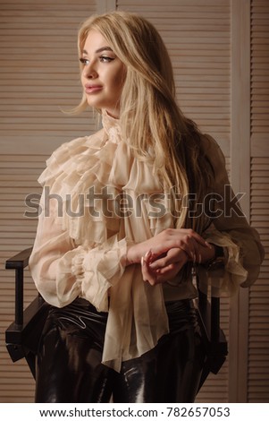 Beautiful blond woman with curly hair and cream top sitting on a wood chair in photo studio