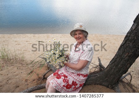 Beautiful blond woman in a hat and white with a pink pattern dress with a bouquet of daisies on the shore of the pond