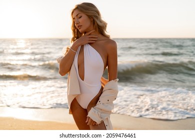 Beautiful blond woman in sexy swimwear posing on the beach in sunset light. Prtfect wavy hairs, tan skim body. Summer tropical mood. 