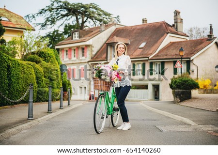Beautiful blond woman standing next to mint color bicycle with big colorful bouquet of flowers in basket